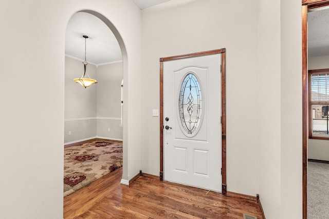 foyer featuring arched walkways, crown molding, baseboards, and wood finished floors