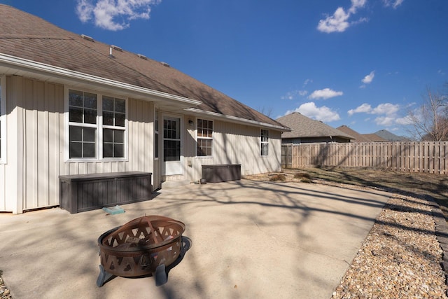 rear view of property featuring roof with shingles, fence, a fire pit, and a patio