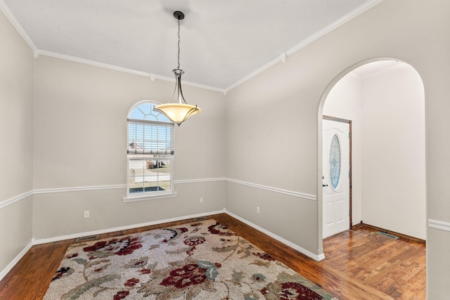 foyer featuring baseboards, arched walkways, wood finished floors, and ornamental molding