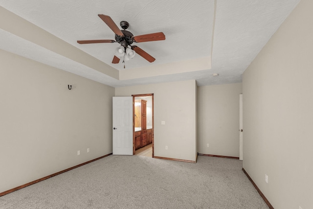 unfurnished bedroom featuring light carpet, baseboards, a raised ceiling, and a textured ceiling