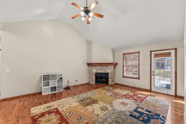 living area with vaulted ceiling, a stone fireplace, wood finished floors, and a ceiling fan