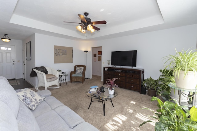 carpeted living room featuring a raised ceiling and ceiling fan