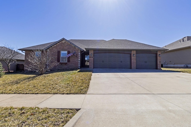 single story home featuring driveway, brick siding, a shingled roof, an attached garage, and a front yard