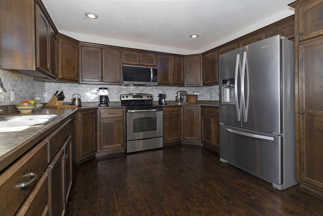 kitchen with dark brown cabinetry, tasteful backsplash, dark countertops, dark wood-style floors, and stainless steel appliances