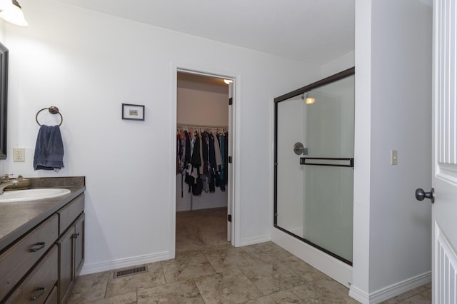 bathroom with vanity, baseboards, visible vents, a stall shower, and a walk in closet