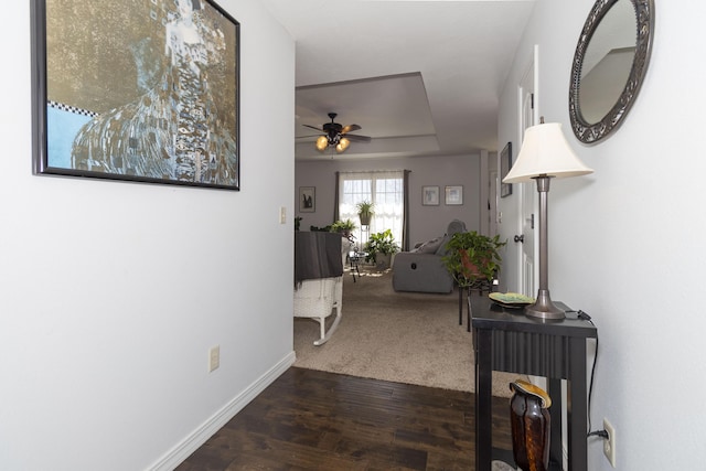 corridor with baseboards, a tray ceiling, and dark wood-style flooring