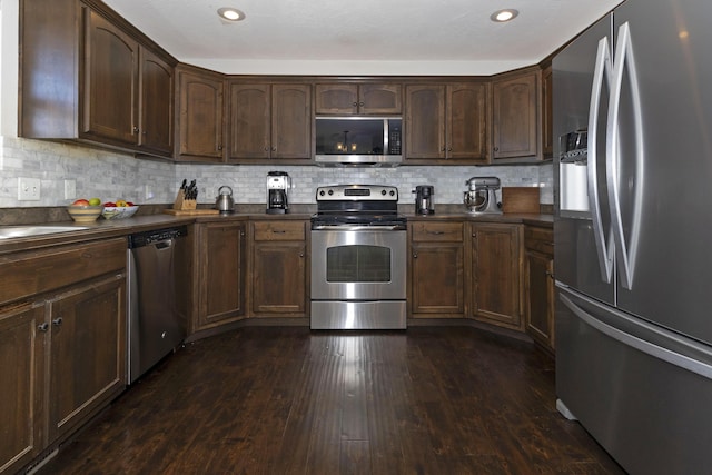 kitchen featuring dark countertops, dark wood-style floors, tasteful backsplash, and stainless steel appliances