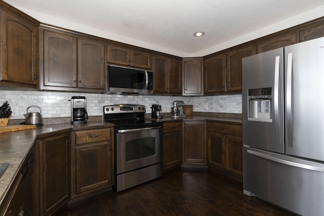 kitchen featuring dark wood finished floors, dark countertops, appliances with stainless steel finishes, dark brown cabinets, and backsplash