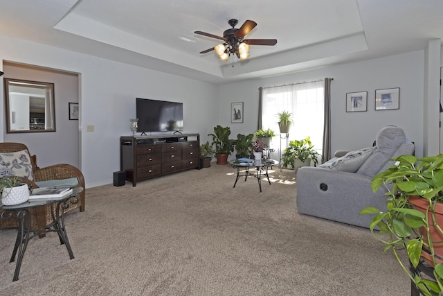 living room featuring light carpet, ceiling fan, a raised ceiling, and baseboards