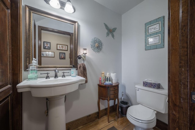 half bath with baseboards, toilet, and wood finished floors