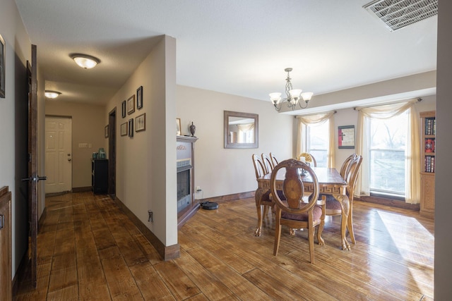 dining area featuring baseboards, visible vents, dark wood finished floors, a fireplace, and a notable chandelier