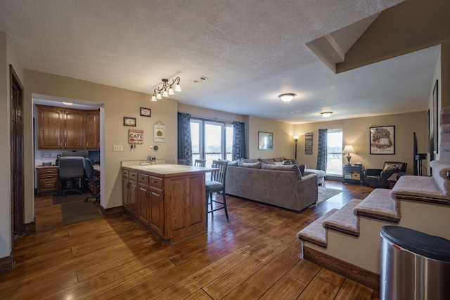 kitchen featuring dark wood-style flooring, built in desk, open floor plan, a textured ceiling, and a kitchen bar