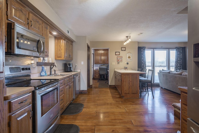 kitchen featuring stainless steel appliances, dark wood-type flooring, a sink, a kitchen breakfast bar, and open floor plan