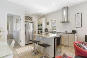 212 W Main St, Branson, MO 65616 - kitchen featuring stainless steel appliances, wall chimney range hood, a kitchen bar, and light wood-style floors