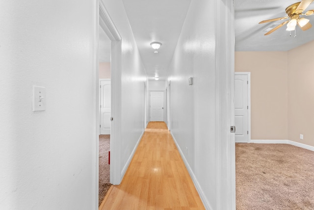 corridor with light carpet, light wood-style flooring, and baseboards