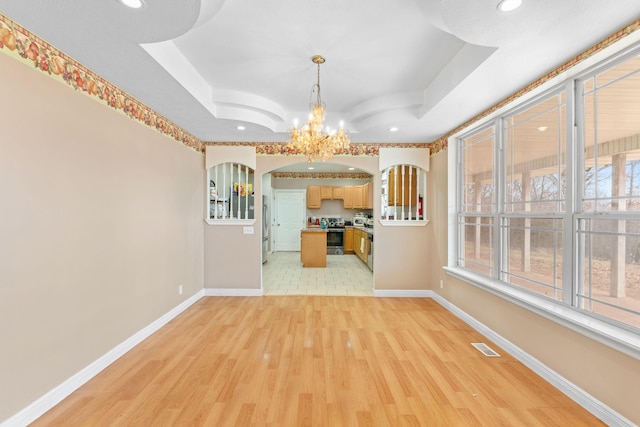 unfurnished dining area featuring light wood-style floors, a tray ceiling, and baseboards