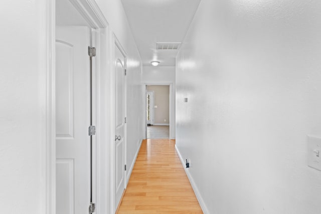 corridor featuring light wood-style flooring, visible vents, and baseboards