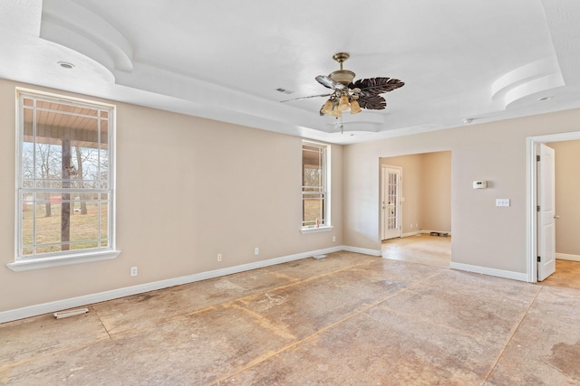 empty room featuring a tray ceiling, visible vents, ceiling fan, and baseboards