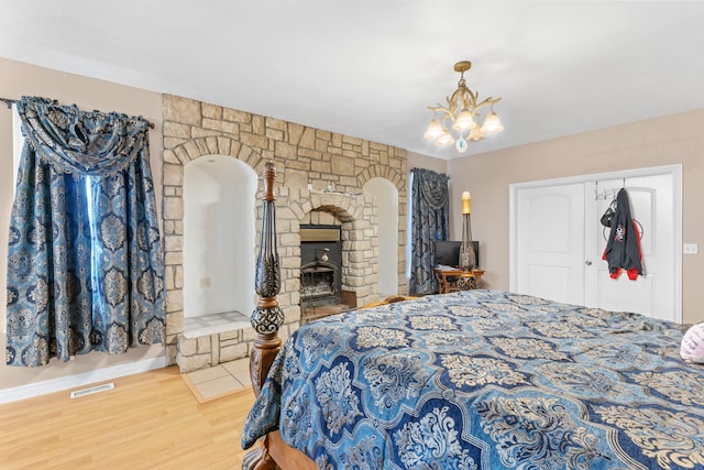 bedroom featuring arched walkways, a stone fireplace, wood finished floors, visible vents, and an inviting chandelier