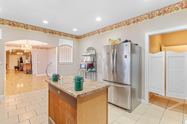 kitchen with arched walkways, a center island, light tile patterned floors, light countertops, and appliances with stainless steel finishes