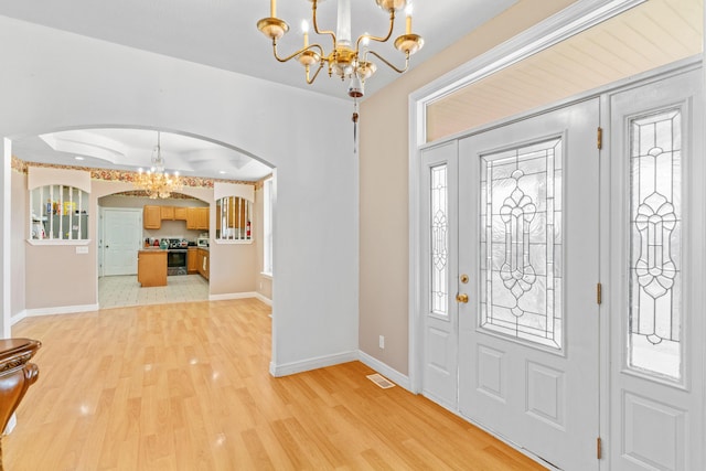 entrance foyer with arched walkways, light wood finished floors, visible vents, a chandelier, and baseboards