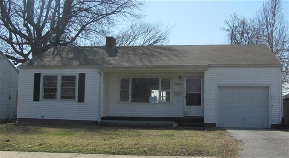 single story home featuring a front lawn, a chimney, an attached garage, and aphalt driveway