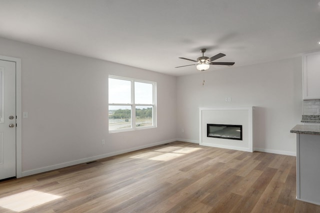 unfurnished living room with light wood finished floors, visible vents, a ceiling fan, a glass covered fireplace, and baseboards