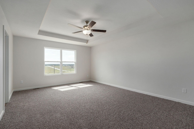 empty room featuring carpet, a raised ceiling, ceiling fan, and baseboards