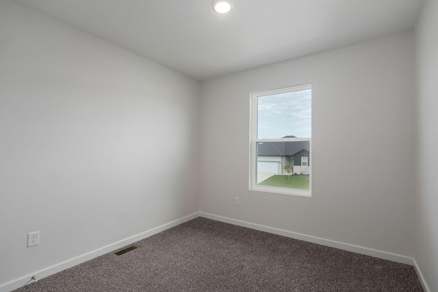 empty room featuring visible vents, dark carpet, and baseboards