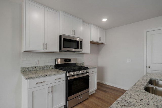 kitchen with light stone counters, wood finished floors, white cabinetry, appliances with stainless steel finishes, and backsplash