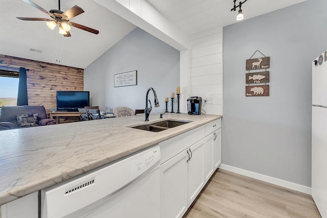 kitchen featuring wooden walls, visible vents, an accent wall, white dishwasher, and a sink