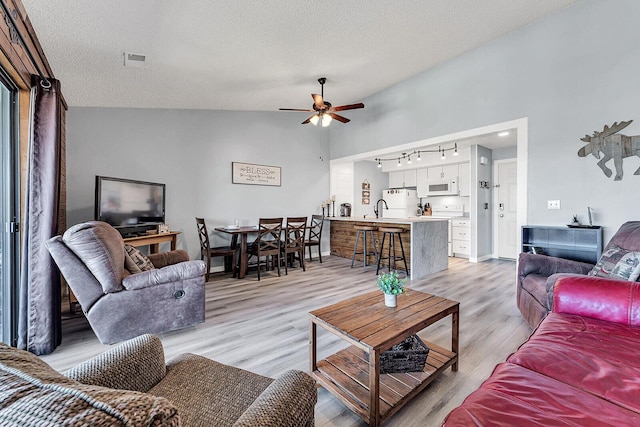 living room with light wood finished floors, a ceiling fan, rail lighting, vaulted ceiling, and a textured ceiling