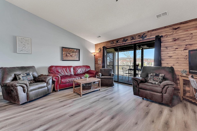 living room with visible vents, wood walls, a textured ceiling, wood finished floors, and high vaulted ceiling