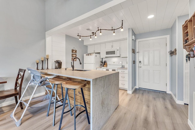 kitchen featuring a peninsula, white appliances, a breakfast bar, a sink, and white cabinetry