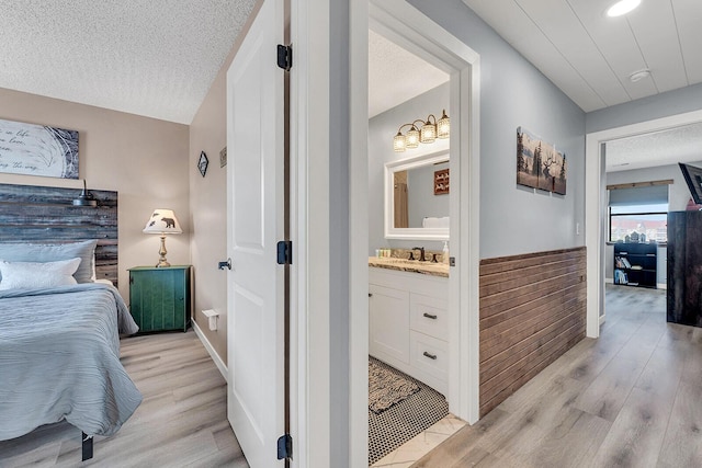 bedroom featuring a textured ceiling, a sink, baseboards, light wood finished floors, and ensuite bath