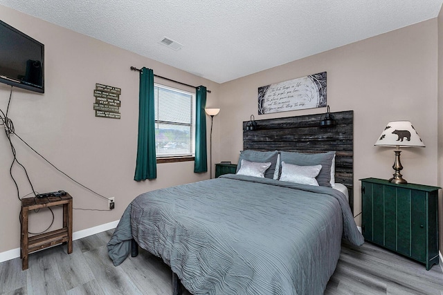 bedroom featuring a textured ceiling, wood finished floors, visible vents, and baseboards