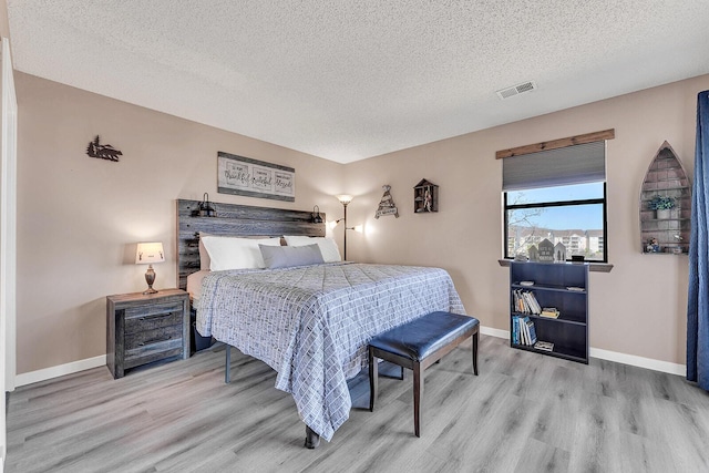 bedroom with baseboards, a textured ceiling, visible vents, and wood finished floors