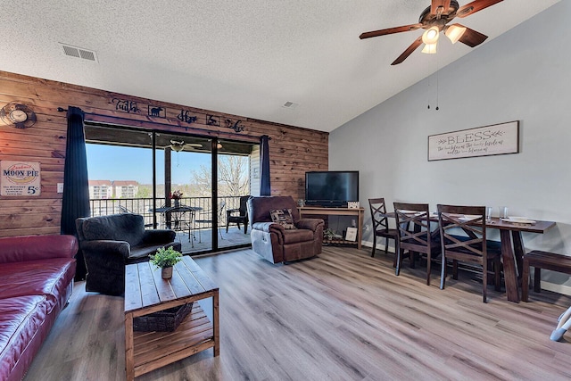 living room featuring wood walls, a textured ceiling, visible vents, and wood finished floors