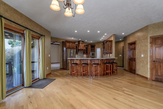 kitchen featuring a kitchen breakfast bar, light countertops, appliances with stainless steel finishes, custom exhaust hood, and light wood finished floors