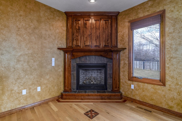 room details with baseboards, a tiled fireplace, visible vents, and wood finished floors