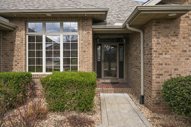 entrance to property with a shingled roof and brick siding