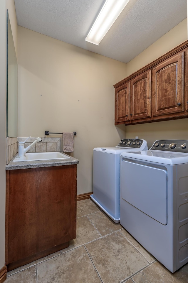 laundry room featuring cabinet space, a textured ceiling, washer and clothes dryer, and a sink