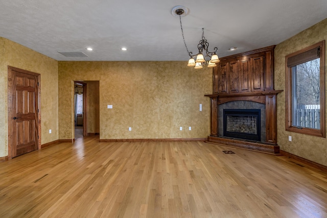 unfurnished living room with a fireplace, visible vents, light wood-style flooring, a chandelier, and baseboards