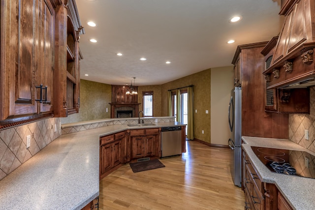 kitchen with light wood finished floors, a peninsula, stainless steel appliances, open shelves, and a sink