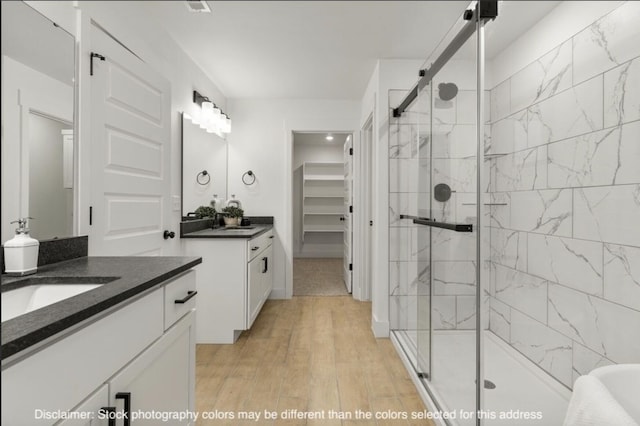 bathroom with a sink, a stall shower, two vanities, and wood finished floors