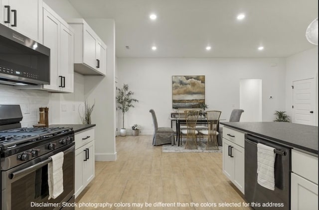 kitchen featuring white cabinets, dark countertops, stainless steel appliances, light wood-type flooring, and backsplash