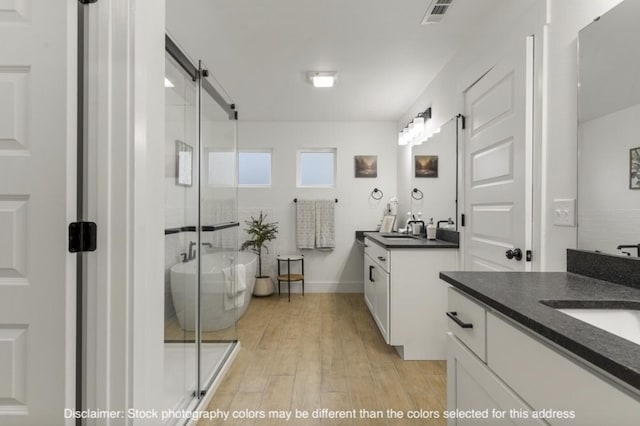 bathroom featuring wood finished floors, two vanities, visible vents, a soaking tub, and a stall shower