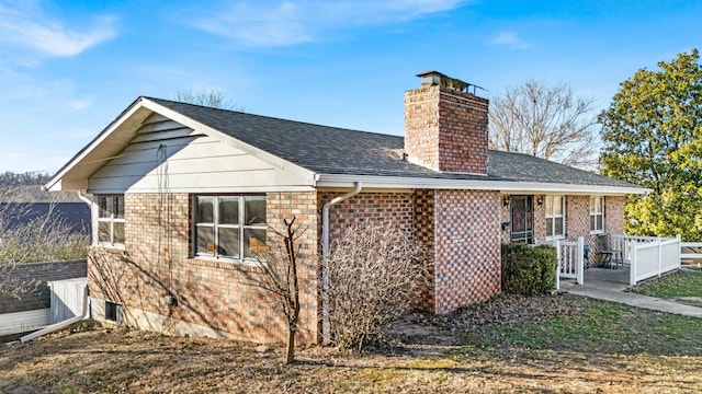 rear view of property with roof with shingles, brick siding, and a chimney