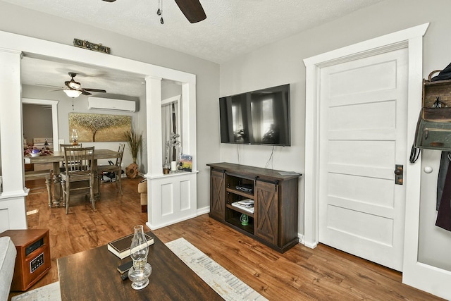 living room featuring ceiling fan, an AC wall unit, decorative columns, and wood finished floors