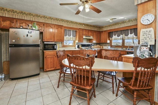 kitchen featuring black microwave, under cabinet range hood, white range with gas cooktop, freestanding refrigerator, and brown cabinetry